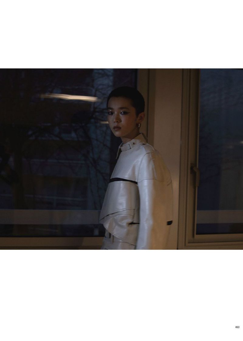Model with short hair wearing a white jacket standing indoors near a dark window for Pop Magazine editorial.