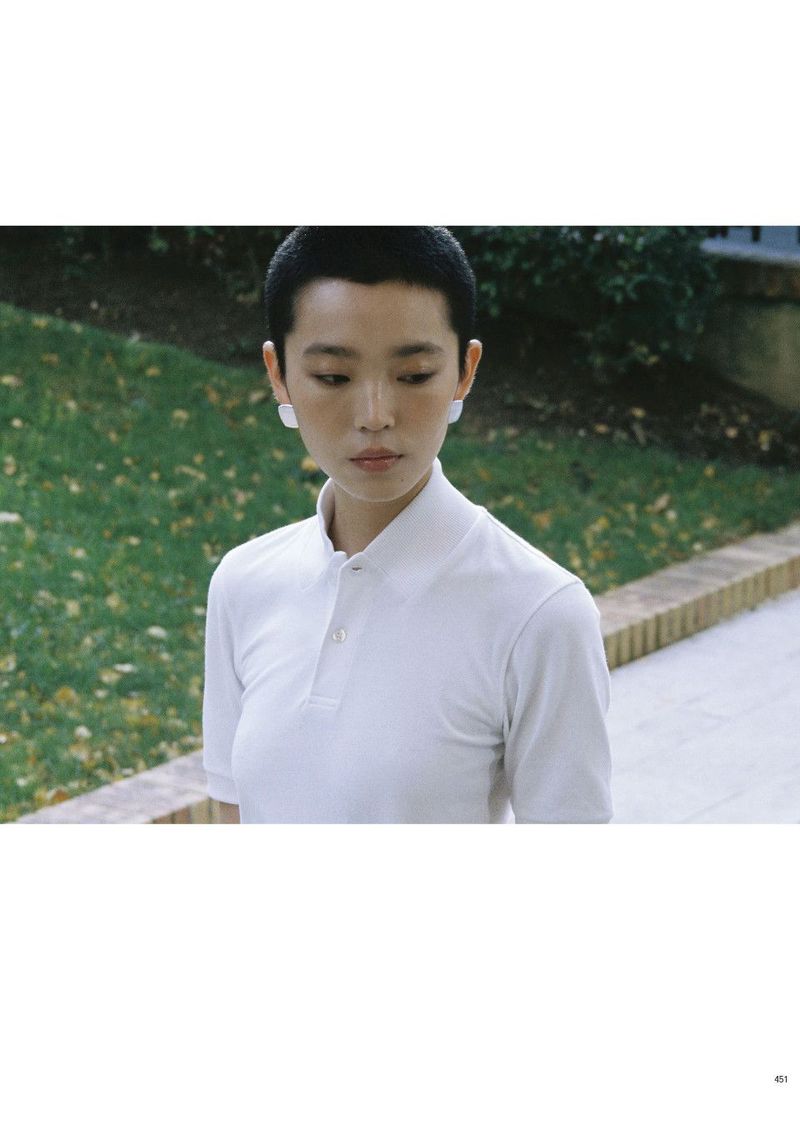 Model with short dark hair wearing a white polo shirt outdoors in a garden setting for Pop Magazine editorial.