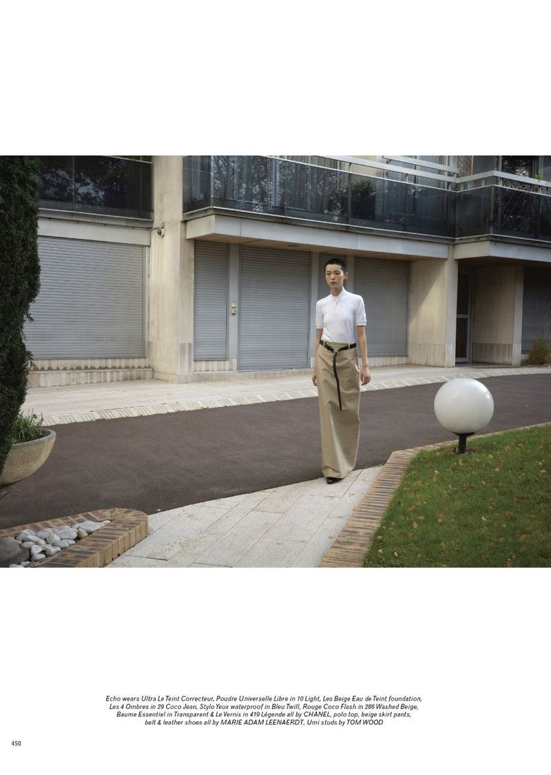 Model wearing a white polo top and beige skirt pant standing outside a residential building for Pop Magazine editorial.