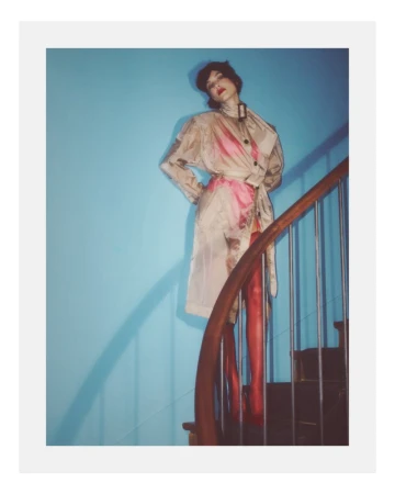 Alexa Chung standing on a spiral staircase in a patterned coat and red tights against a blue wall