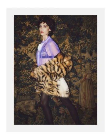 Alexa Chung wearing a sheer purple top and faux fur coat against an ornate tapestry background