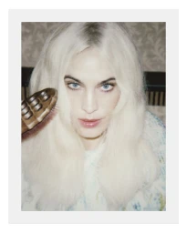 Close-up portrait of Alexa Chung holding a hairbrush near her shoulder with patterned wallpaper in the background.