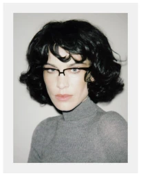 Portrait of Alexa Chung wearing black glasses and grey turtleneck against a white background