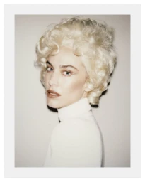 Portrait of Alexa Chung with voluminous blonde vintage hairstyle wearing a white turtleneck against a neutral backdrop