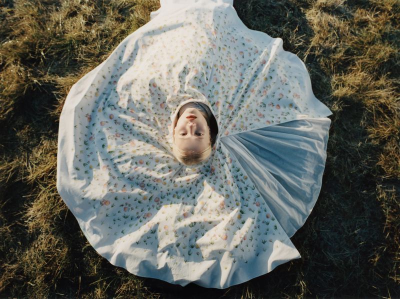 Model lying on grass with a wide circular patterned skirt fanned out around her face in an overhead portrait shot