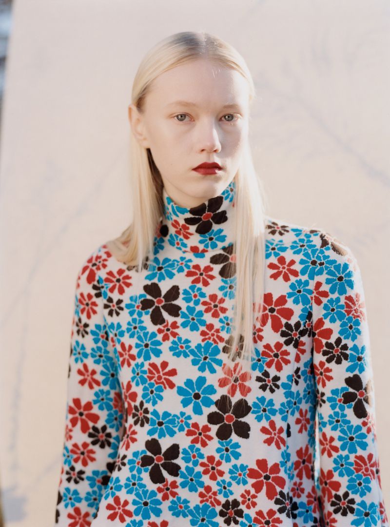 Model with long blonde hair wearing a floral turtleneck sweater in red and blue for Achtung Magazine editorial.