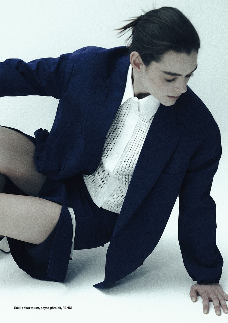 Model in a dark navy blazer and white collared shirt seated against a plain white studio background.