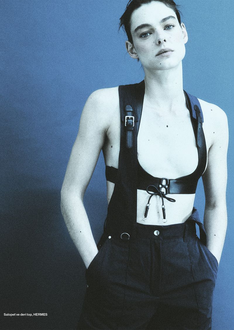 Model wearing dark overalls and a leather harness against a solid blue background for Numéro Istanbul editorial