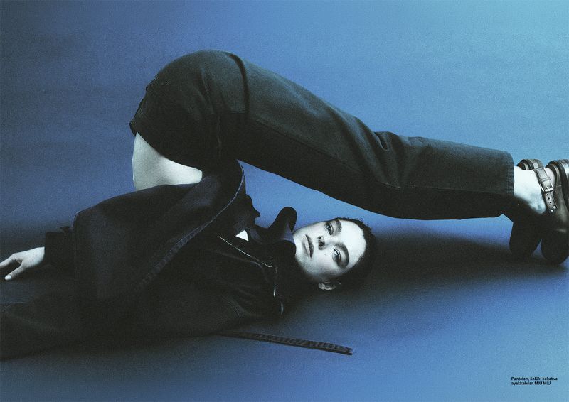 Model lying on back in a flexible pose wearing dark trousers and shoes against a blue studio background for Numéro Istanbul