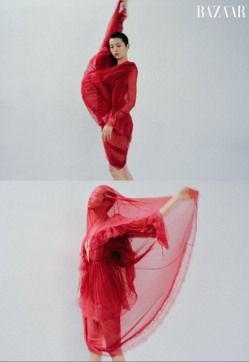 Model in a flowing red sheer dress with arms raised against a plain white studio background