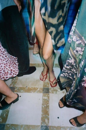 Close-up shot of people standing on a tiled floor wearing summer footwear including red flip-flops and sandals.