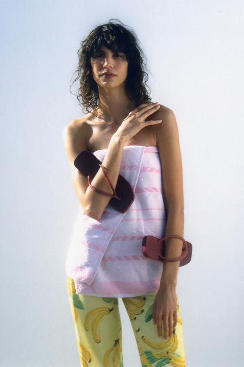 Model Mica Argañaraz in a white and pink striped towel and banana print trousers holding sandals for Zara x Havaianas