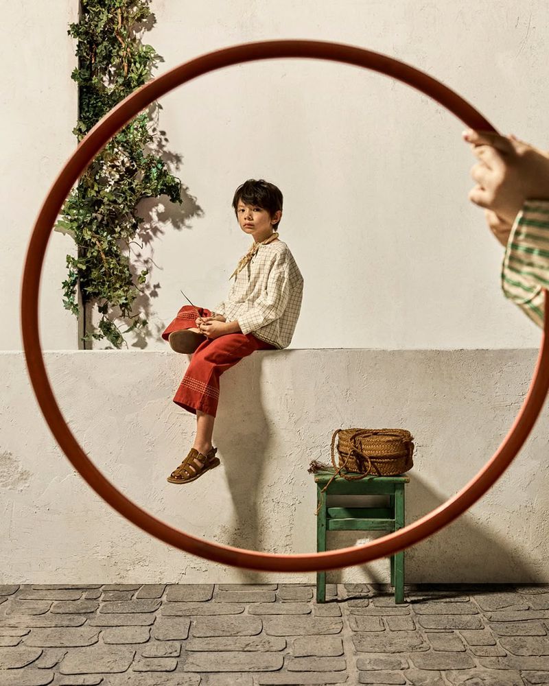 A young boy seated on a low white wall, framed through a large circular ring held up in the foreground.