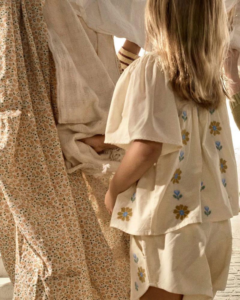 Child wearing cream top and shorts with floral embroidery standing beside patterned fabric in Zara Kids campaign