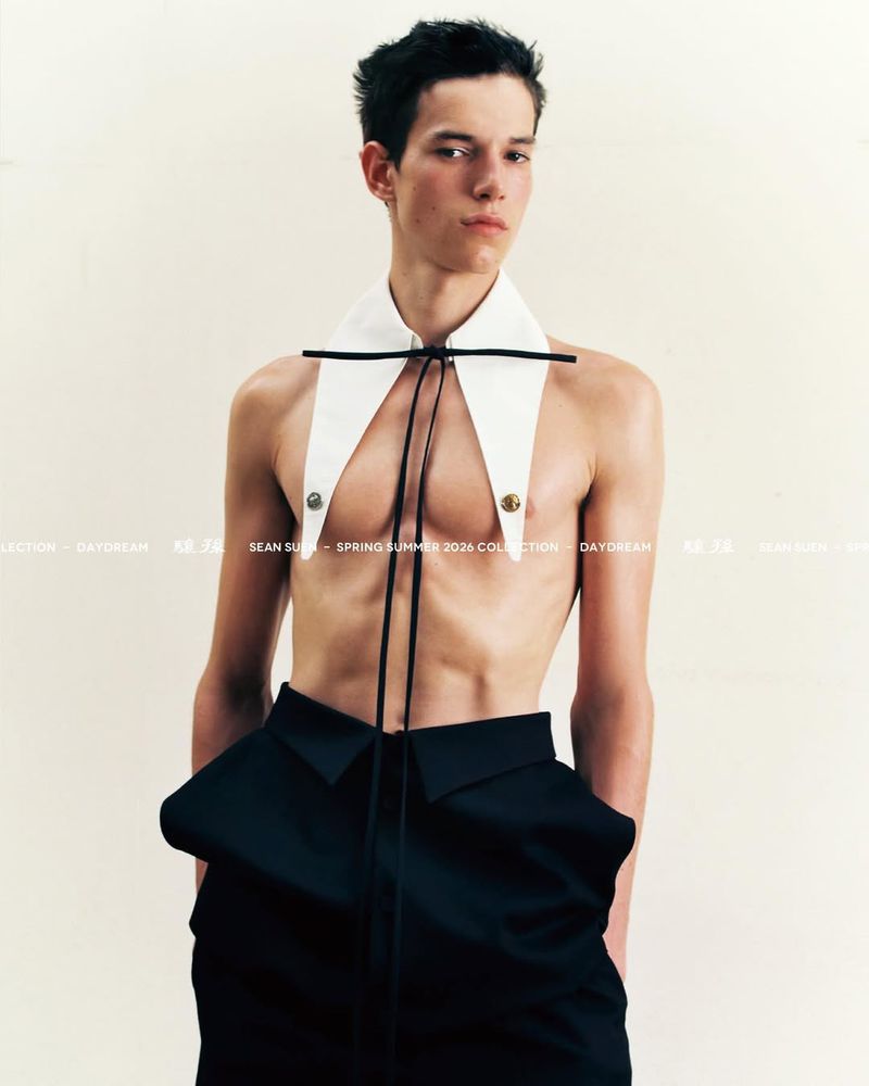 A male model wearing a detachable white shirt collar and black trousers against a neutral background.