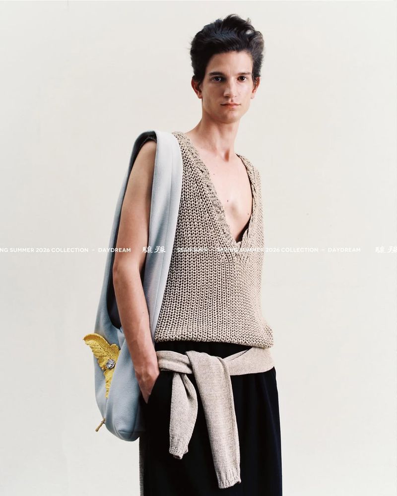 Model wearing an open-weave knit vest and carrying a light blue bag against a plain background for Sean Suen