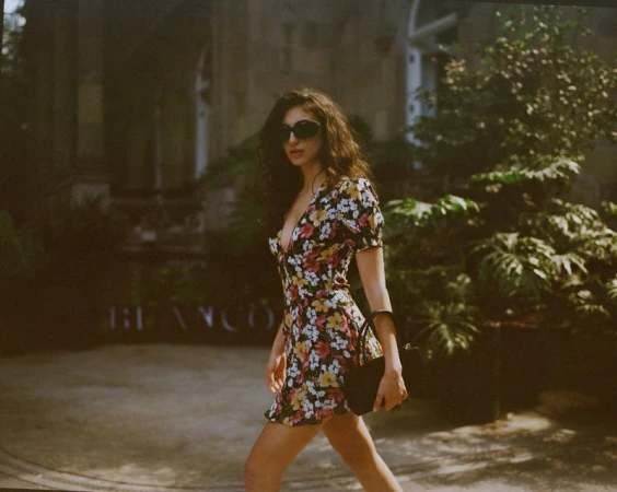 Model wearing a floral print mini dress and sunglasses holding a black handbag outdoors
