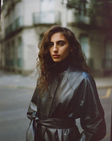 Model wearing a black leather belted coat standing on a city street for Reformation Spring 2026.