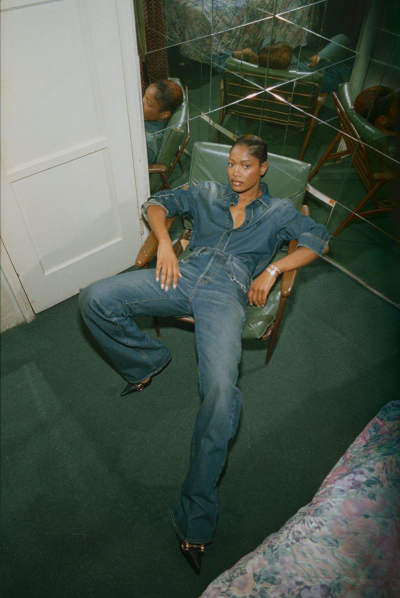 Keke Palmer seated in a green armchair wearing a denim jumpsuit against a green carpet and mirrored wall