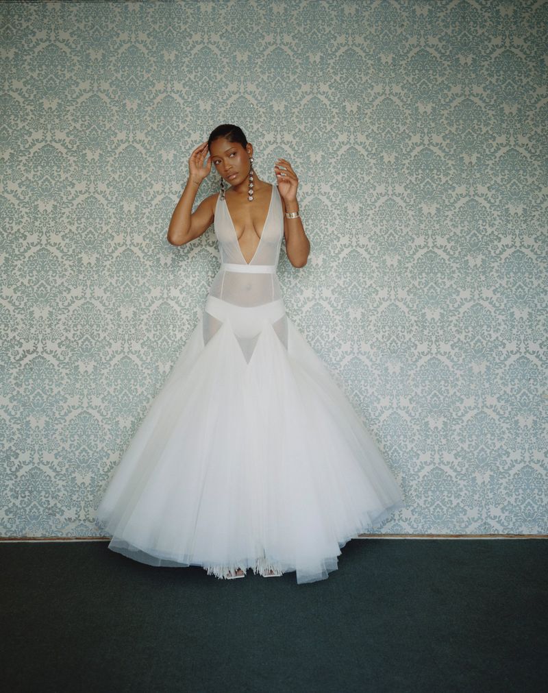 Keke Palmer in a white sheer gown standing against a patterned damask wallpaper background for Cultured Magazine