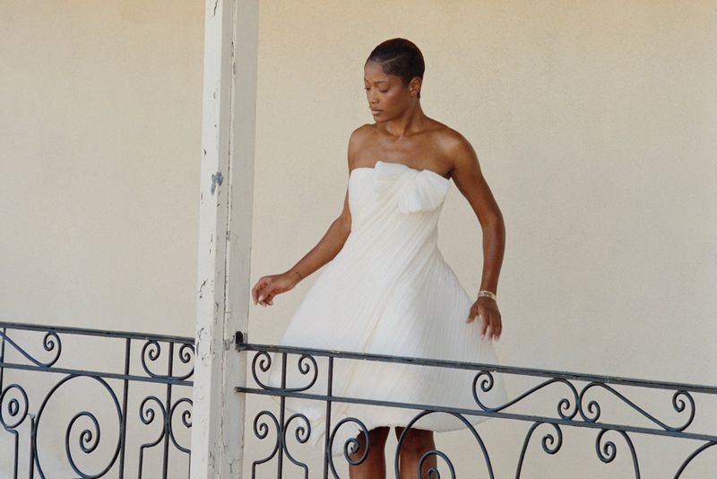 Keke Palmer wearing a white strapless dress behind a wrought iron balcony railing for Cultured Magazine