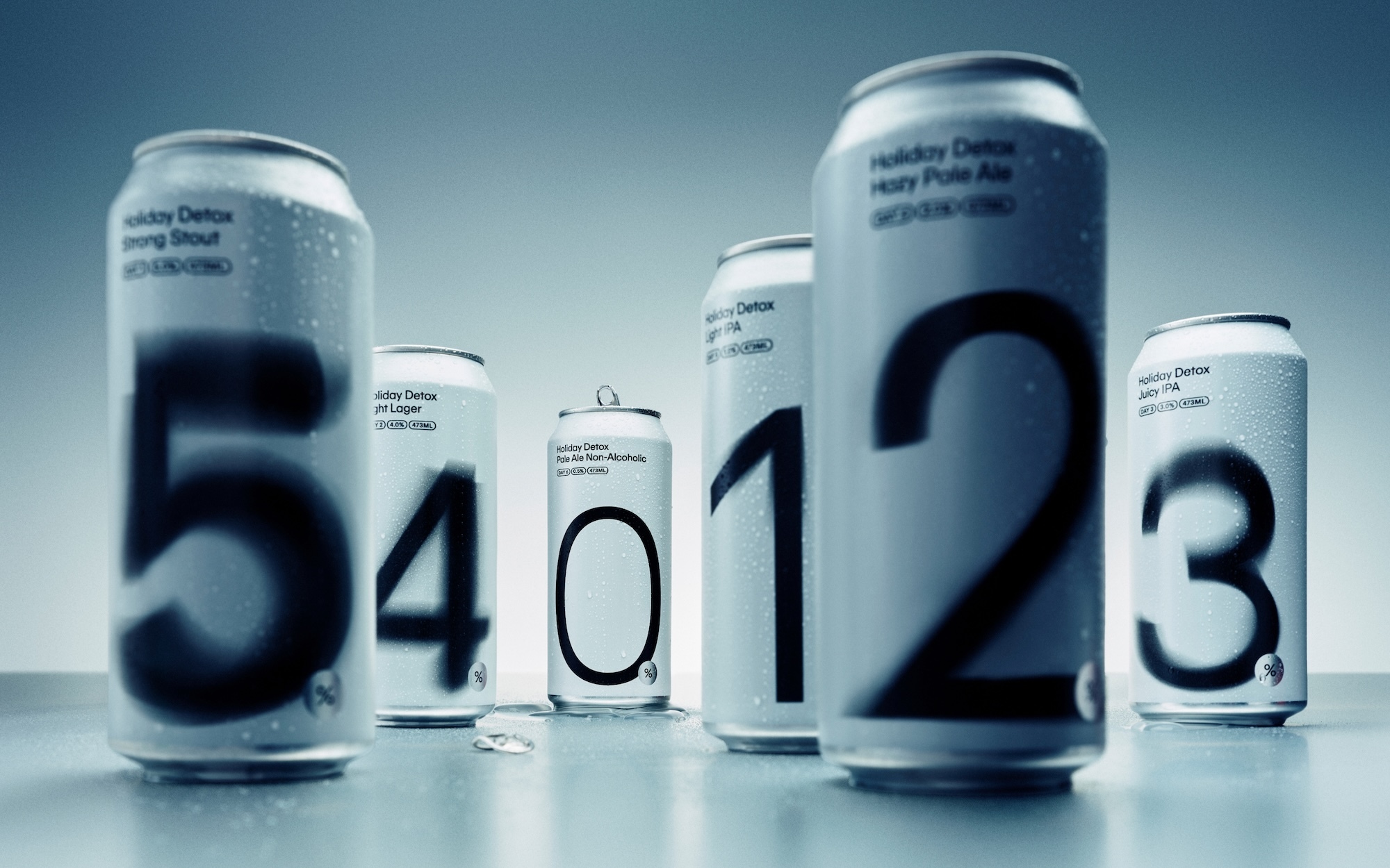 Group of six silver beverage cans with large numbers printed on the side arranged on a reflective surface under soft cool lighting.