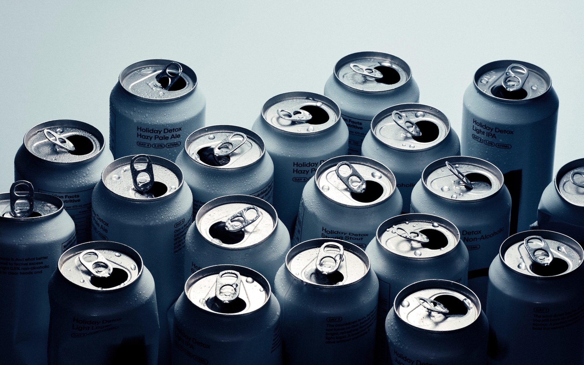 An overhead view of multiple opened beverage cans with condensation droplets against a gradient background.