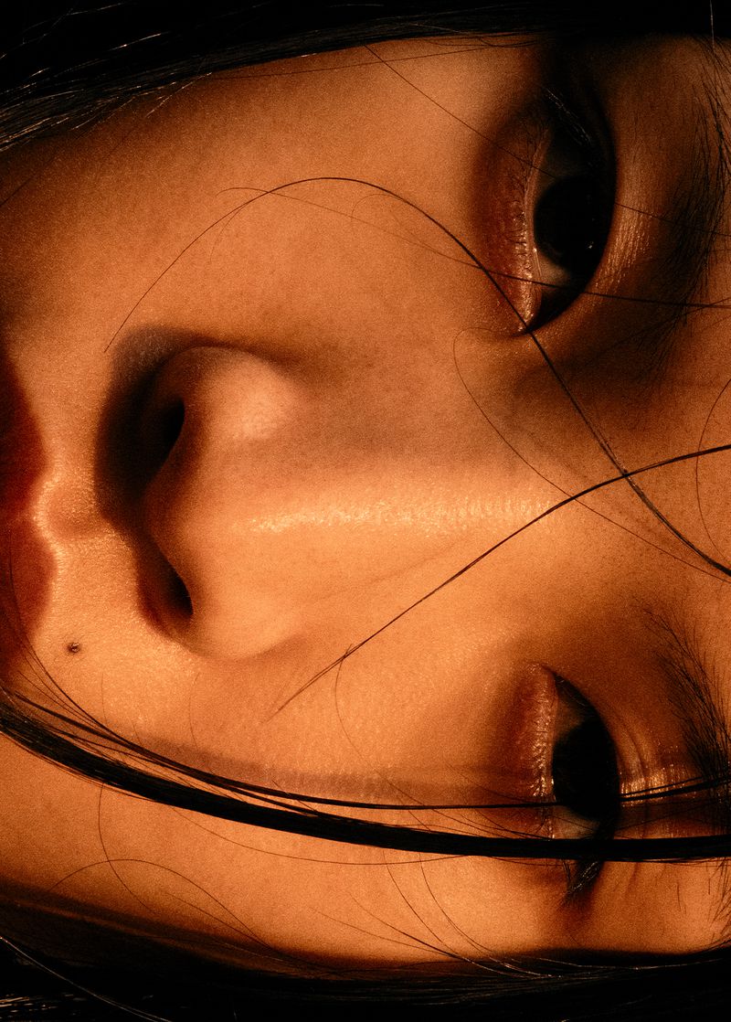 Close-up portrait of a person's face, showcasing skin texture, hair strands, eyes, nose, and a mole, all bathed in warm, diffused lighting.