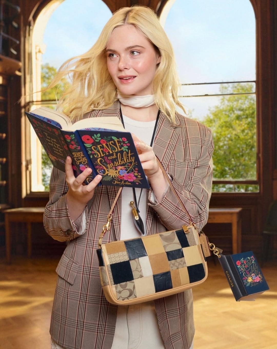 Elle Fanning holding a book and wearing a plaid blazer and patchworked leather shoulder bag inside a library