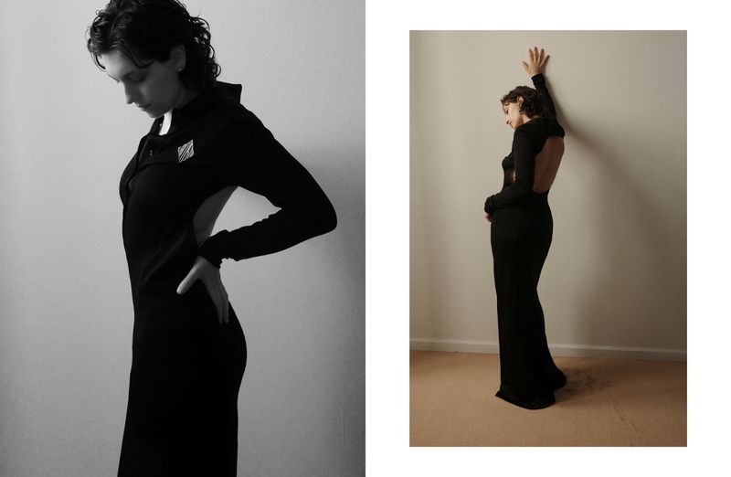 Monochrome portrait of a young woman in a long, dark, form-fitting dress against a neutral backdrop in a photo studio.