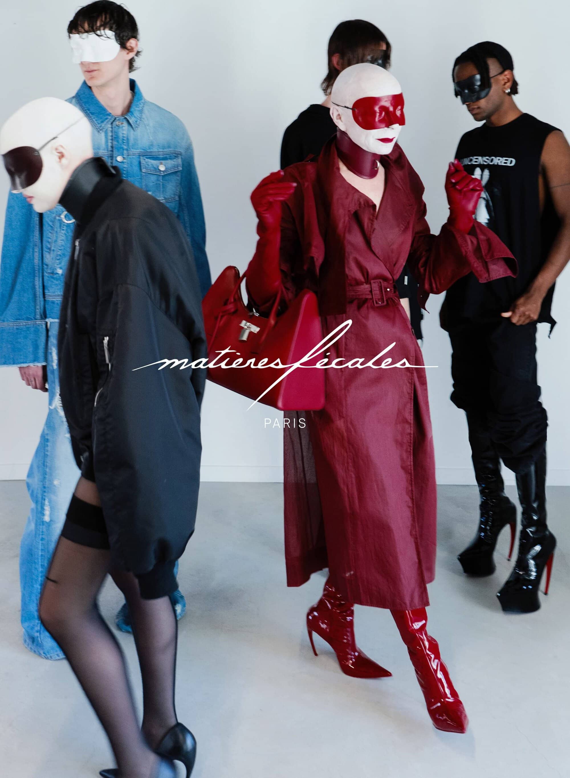 Models in avant-garde attire including red coat and face coverings against a plain white background for Matieres Fecales