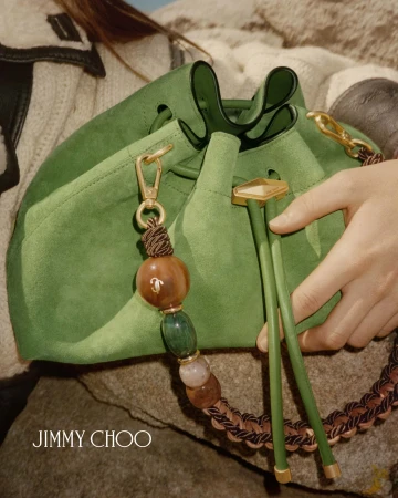 Close-up of a green suede bucket bag with beaded strap held against textured rock and fabric