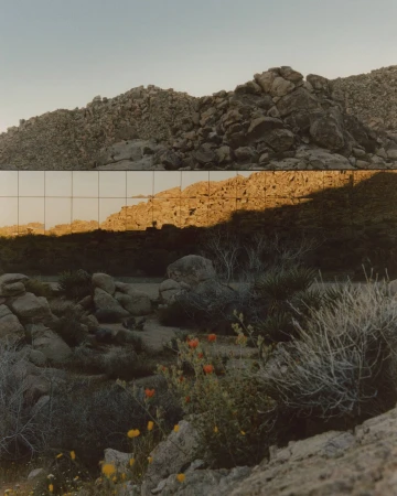 Desert landscape with rocky terrain reflecting in a mirrored glass wall under a clear sky.
