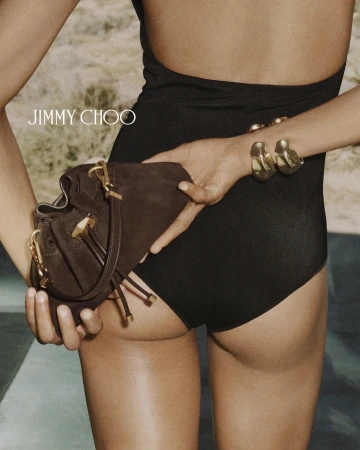 Model in black swimwear holding a brown suede handbag and wearing gold cuff bracelets outdoors