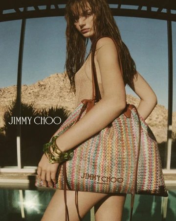 Model carrying a colourful woven shoulder bag outdoors against a desert landscape for Jimmy Choo.