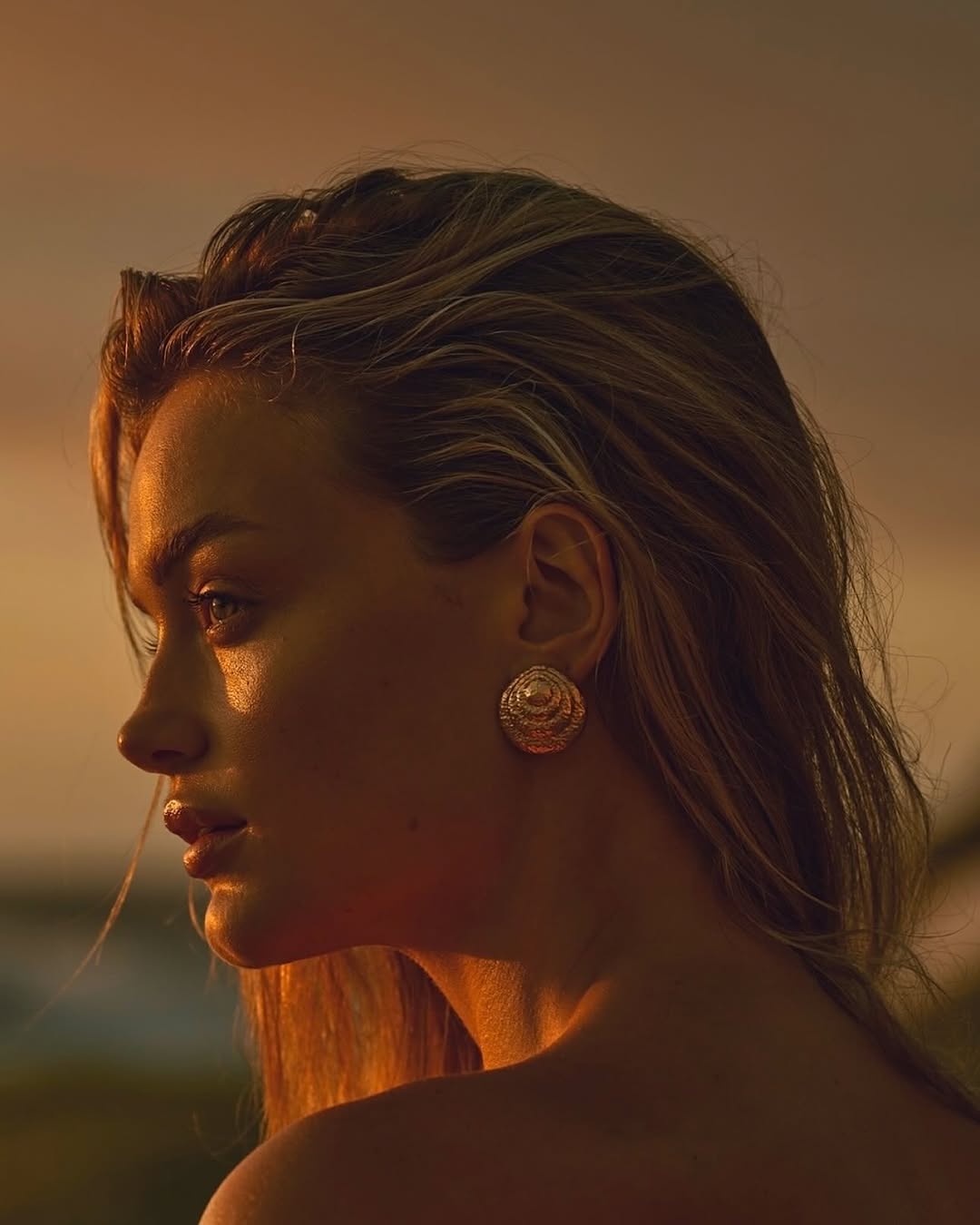 Profile portrait of a blonde adult woman with golden jewelry, illuminated by soft, warm, natural sunlight during golden hour.