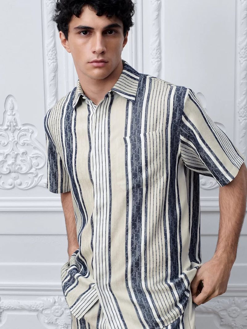 Model wearing a striped short-sleeve button-down shirt against an ornate white paneled wall