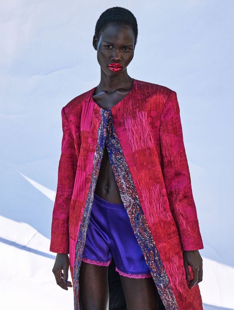 Fashion-forward portrait of an African American woman in a vibrant pink coat and purple shorts against a crisp white backdrop, embodying modern style.