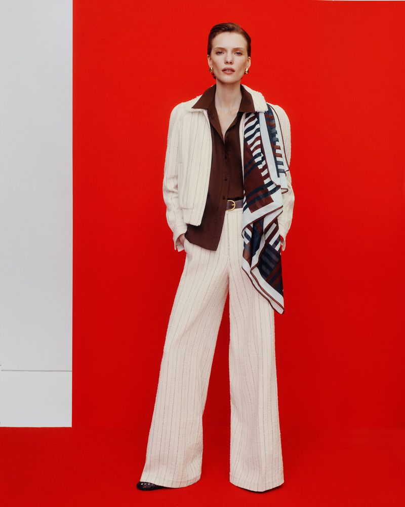 Model standing against a vibrant red backdrop wearing wide trousers and a patterned scarf for ME+EM