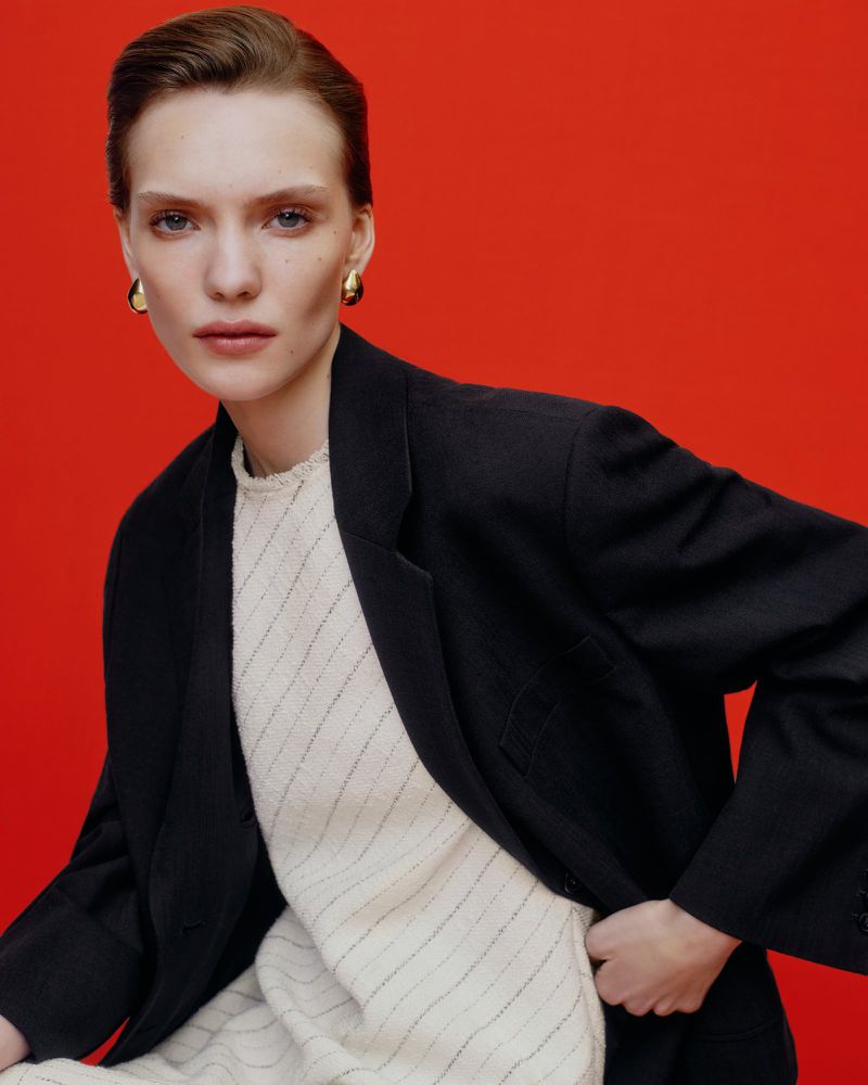 Model in black blazer and cream top against a vibrant red background for ME+EM May campaign