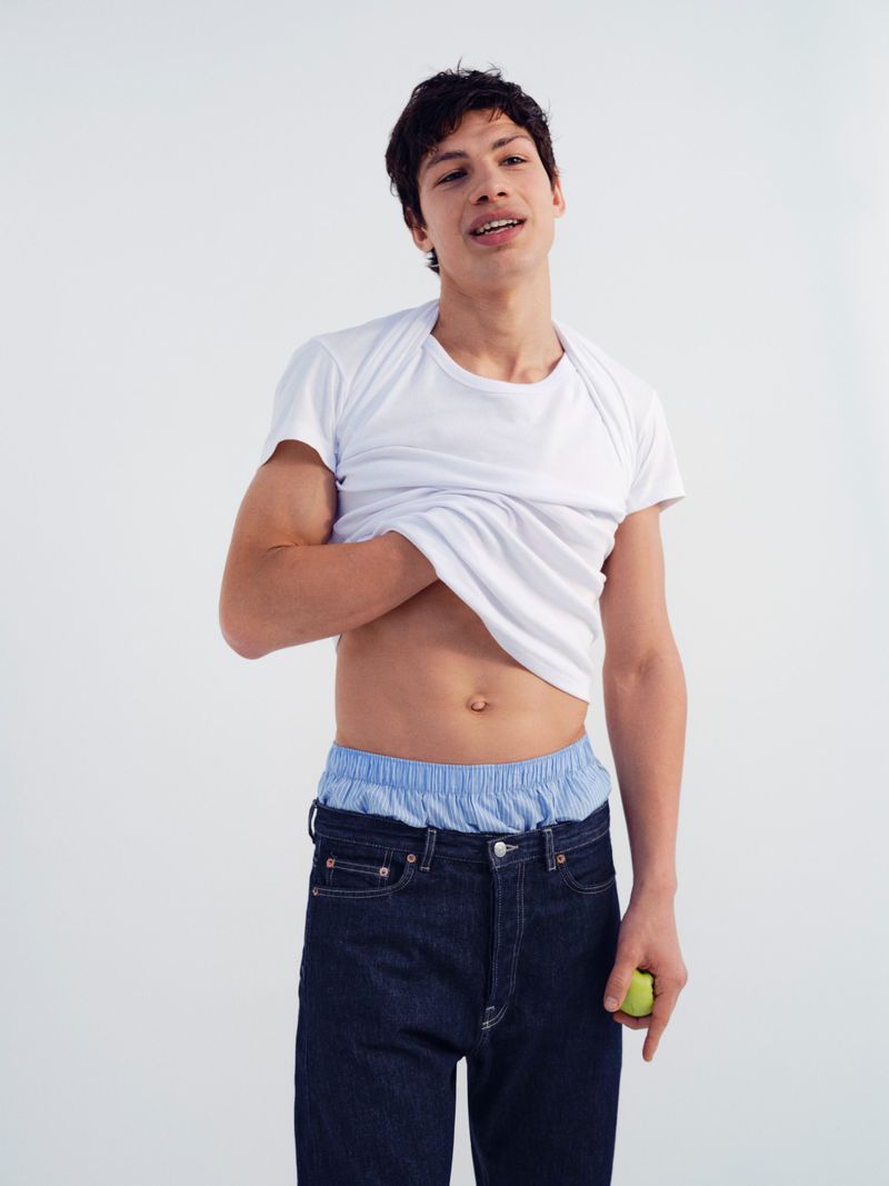 Model Ruben Moreira lifting his white t-shirt against a clean white studio backdrop for Samsoe Samsoe