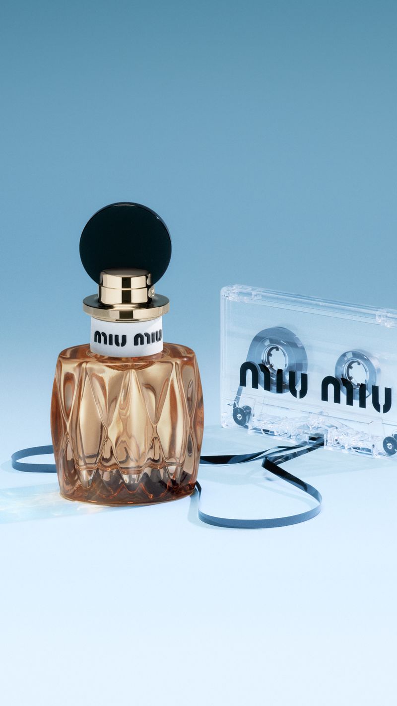 Miu Miu perfume bottle and cassette tape on light blue backdrop in studio lighting for beauty product advertisement.