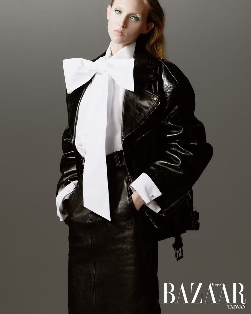 Model Delilah Koch in a black leather jacket and white bow blouse against a grey seamless background for Harper's Bazaar Taiwan.