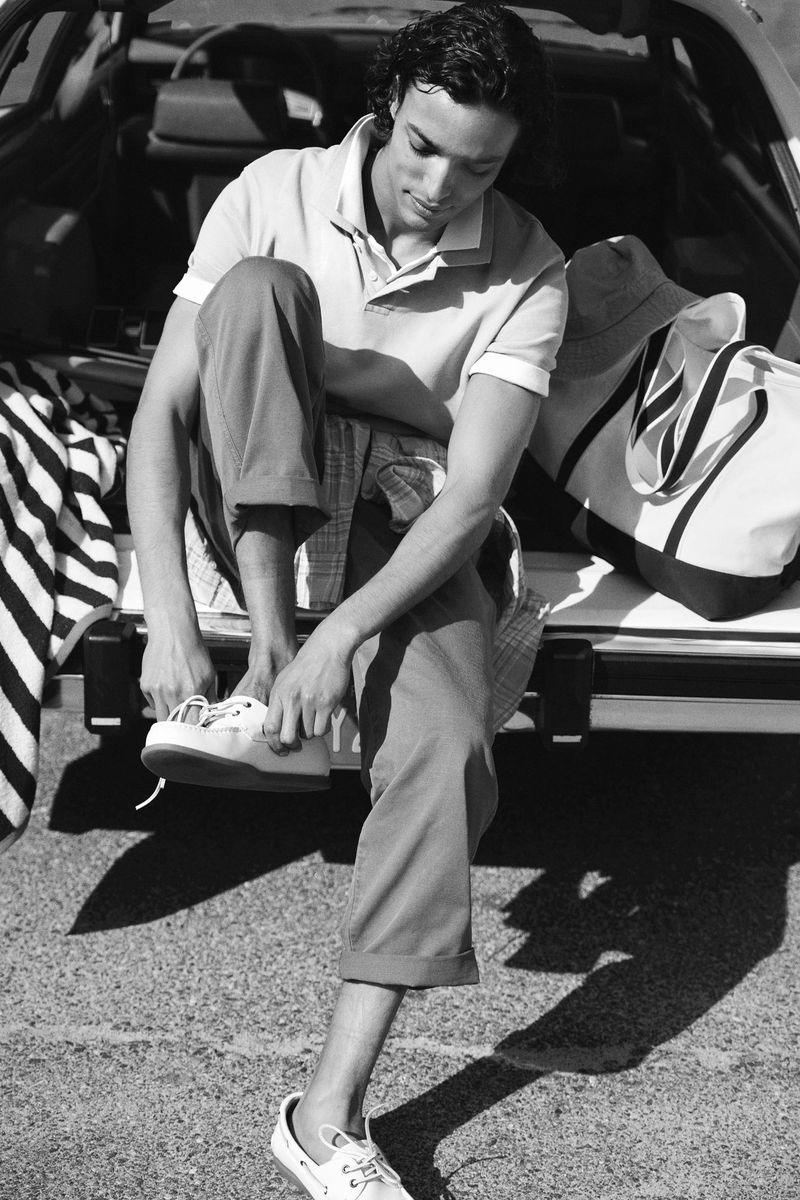 Model sitting on the open back of a car adjusting his shoes in a black and white fashion campaign image