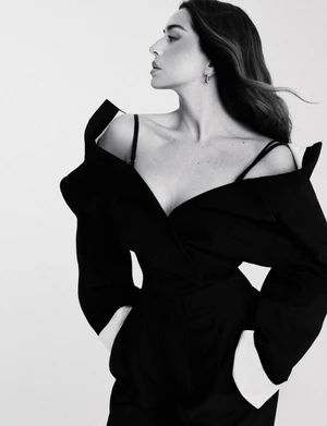 Monochrome fashion editorial portrait of Lola Indigo wearing an oversized off-the-shoulder black jacket against a plain background
