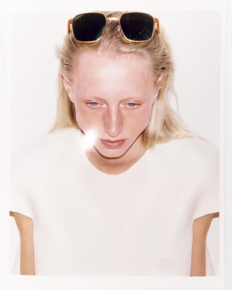 Close-up portrait of a fair-skinned adult woman with blonde hair and sunglasses on her head, against a white background.