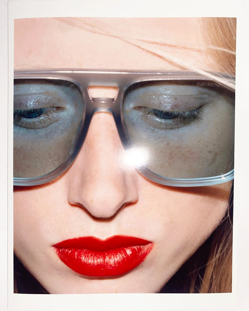 Close-up portrait of a model wearing translucent grey aviator sunglasses and bright red lipstick.