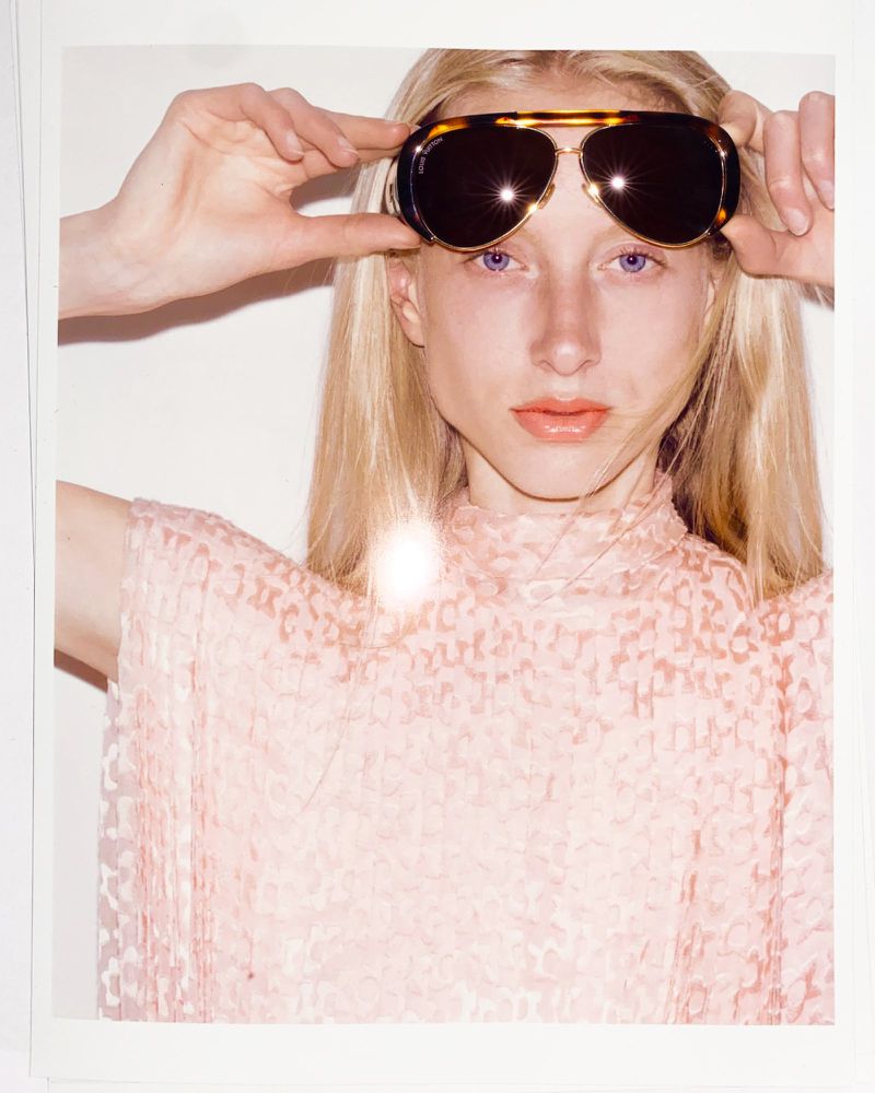 Model wearing tortoiseshell sunglasses and a patterned pink top against a white background