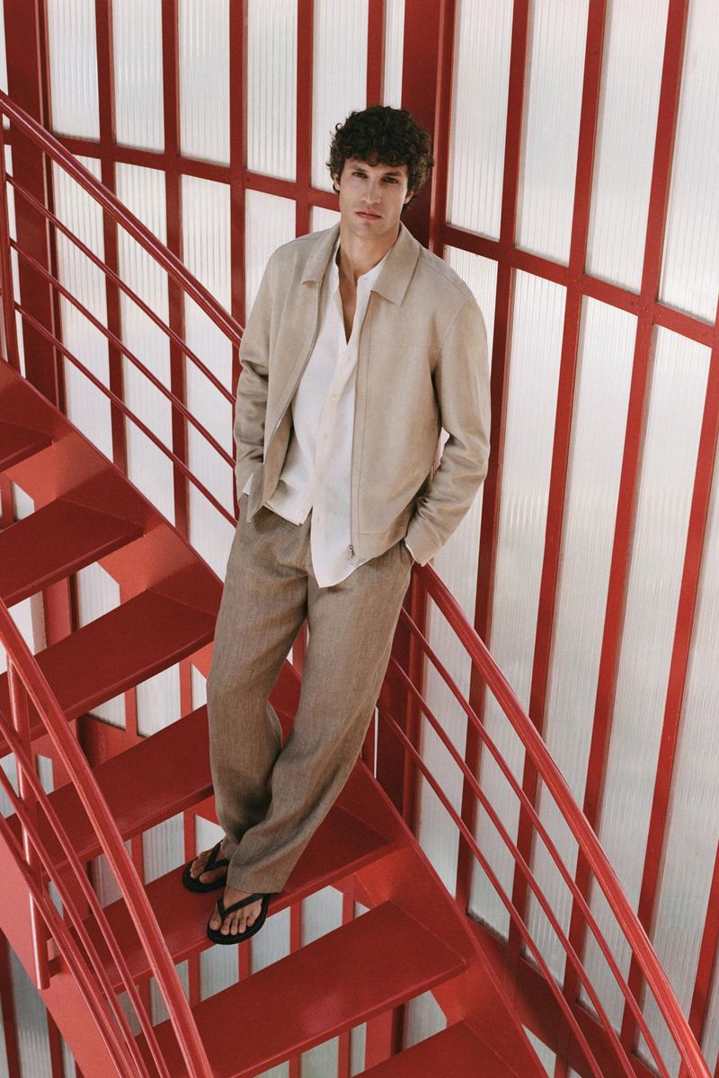 Model standing on red metal stairs wearing a beige jacket over a white shirt and trousers for Massimo Dutti