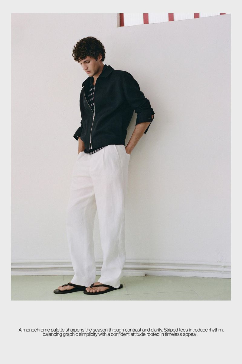 Model Francisco Henriques in a black jacket and white trousers leaning against a white wall for Massimo Dutti